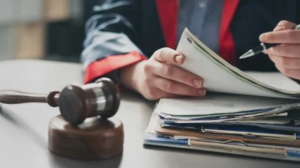 Imagem de um advogado segurando documentos em um escritório de advocacia, com martelo jurídico ao lado, simbolizando o trabalho jurídico e a prática do direito.