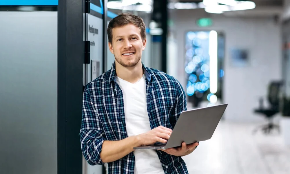 Homem sorridente usando laptop em ambiente de coworking, promovendo tecnologia e inovação