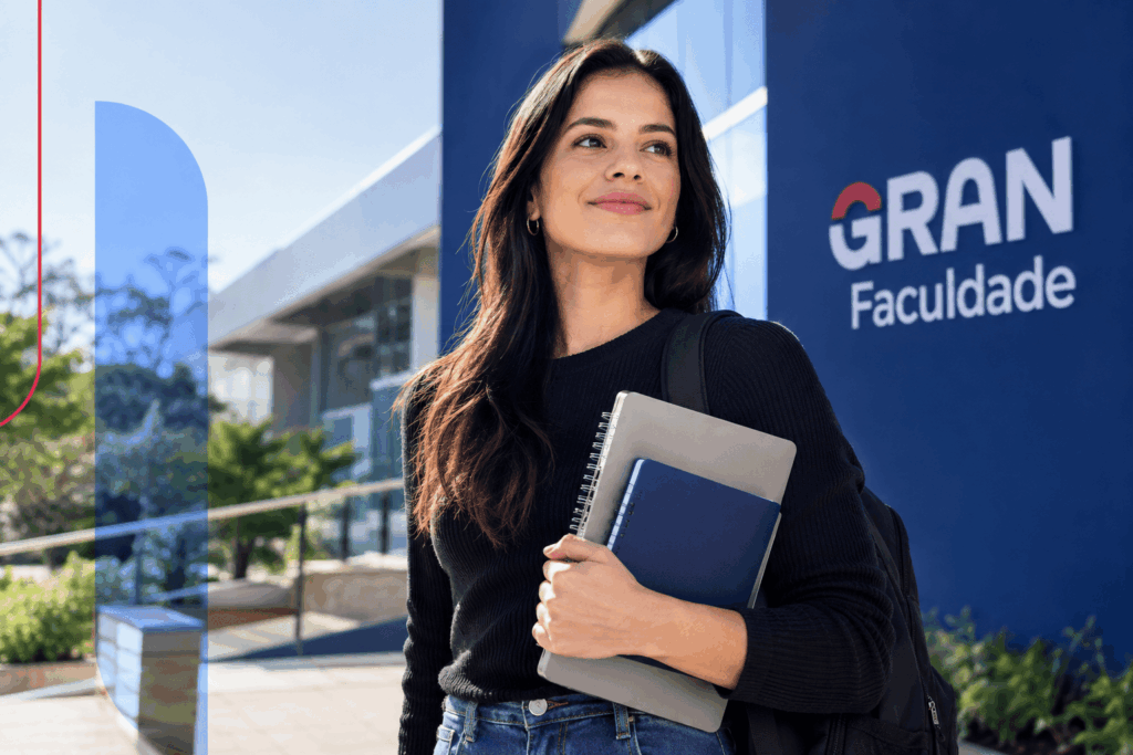 A imagem mostra uma estudante de pé, com mochila e materiais acadêmicos, diante de um ambiente moderno de ensino. O cenário representa a experiência universitária e as possibilidades de formação oferecidas pela Gran Faculdade. A composição transmite profissionalismo, confiança e conexão com a vida acadêmica.